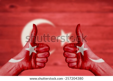 Turkey flag painted on female hands thumbs up with blurry wooden background