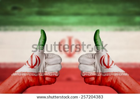 Iran flag painted on female hands thumbs up with blurry wooden background