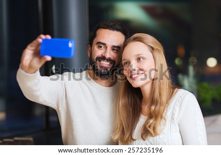 people, leisure, communication, eating and drinking concept - happy couple with smartphone taking selfie at cafe