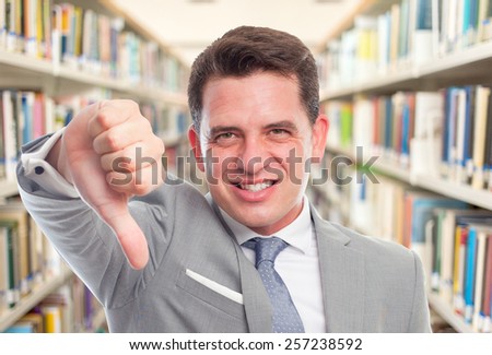 Business man with grey suit. He is looking upset with the thumb down. Over library background