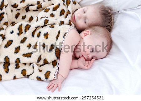Two small children sleeping in an embrace under the spotty blanket