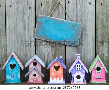 Blank aged wooden sign hanging over row of colorful pastel birdhouses with old weathered wood background