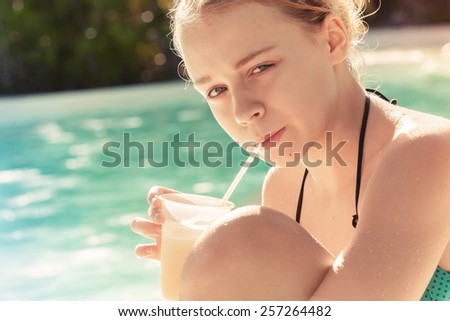 Little blond girl drinks cocktail in swimming pool, vintage toned photo with instagram filter effect