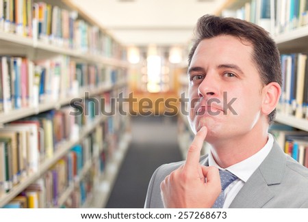 Business man with grey suit. He is poiting to his chin. Over library background