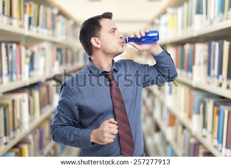Man wearing a blue shirt and red tie. He is drinking from blue bottle. Over library background