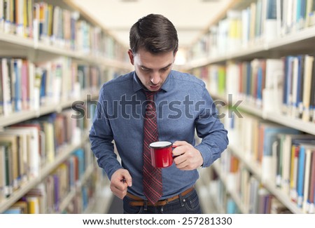 Man wearing a blue shirt and red tie. He is looking surprised into a red cup. Over library background