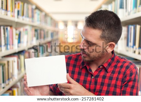 Man with red squares shirt. He is holding a white card. Over library background