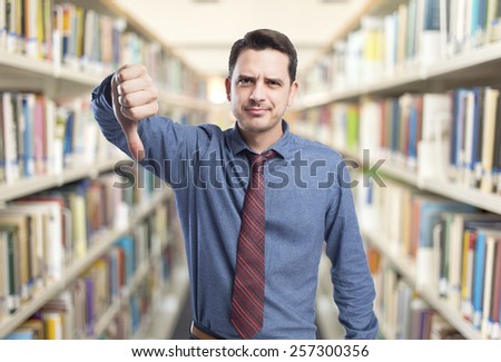 Man wearing a blue shirt and red tie. With the thumb down. Over library background