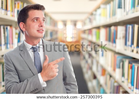 Business man with grey suit. He is pointing to something. Over library background