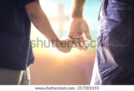 Worship God concept: Child's hand hold father's finger on blurred cross on autumn sunset background Royalty-Free Stock Photo #257301010