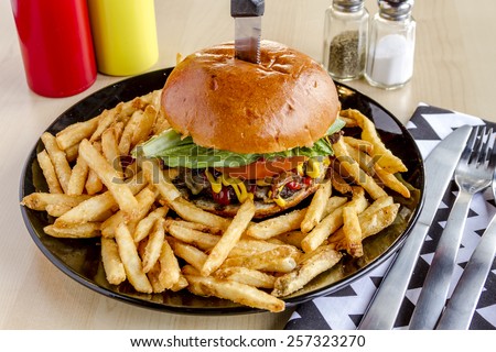 Gourmet pub hamburger with bacon on black plate with french fries sitting on wooden table