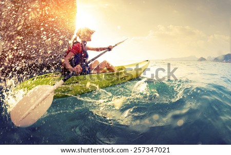 Young lady paddling hard the kayak with lots of splashes near the cliff at sunny day Royalty-Free Stock Photo #257347021