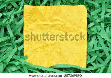 Yellow paper note on green shredded paper 
