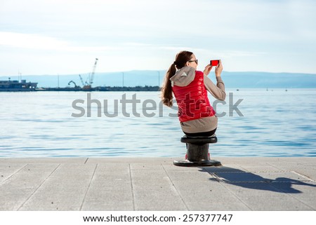Sport woman dressed in warm clothes after the excercnise taking pictures with phone on the promenade in Spring