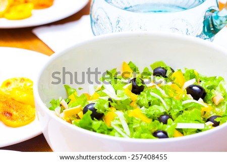 Assorted salad of green leaf lettuce with squid and black olives on lunch table, close up