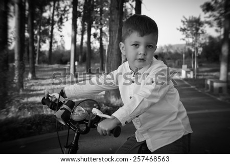 Little boy rides his bicycle in summer afternoon in the park. Nice baby dressed casual. Outdoor black & white  picture.