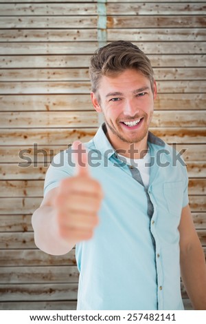 Handsome young man showing thumbs up to camera against wooden background in pale wood