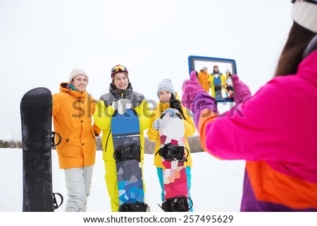 winter sport, technology, leisure, friendship and people concept - happy friends with snowboards and tablet pc computer taking picture outdoors
