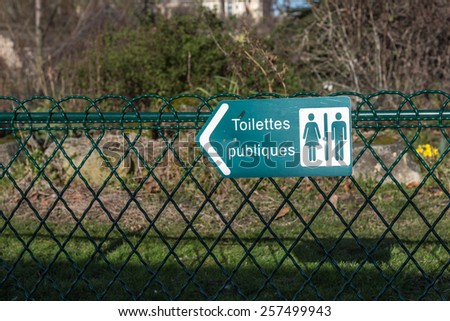 A sign on a green wire fence points the direction to the mens and women's toilets.