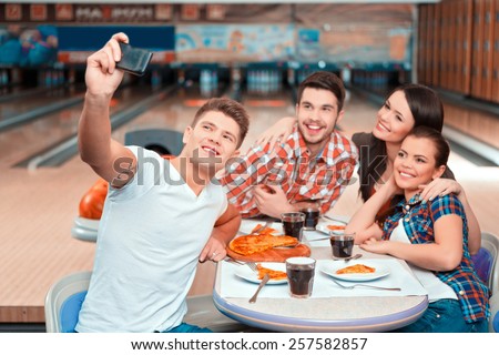 Weekend with friends. Group of cheerful people doing selfie while eating pizza in the bowling club