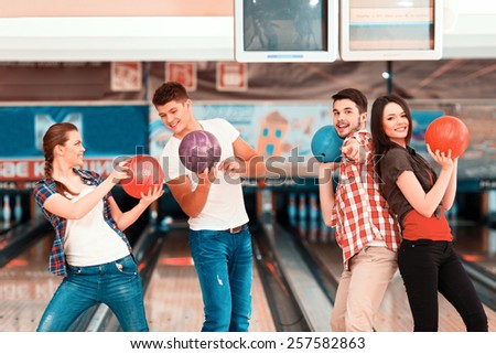 Welcome to the bowling club. Beautiful young people holding bowling balls and posing against bowling alleys