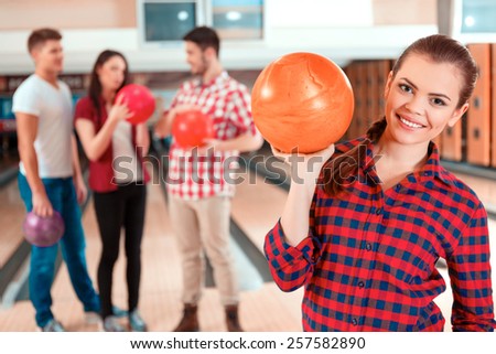 Beautiful and confident player. Beautiful young women holding a bowling ball while three people communicating against bowling alleys