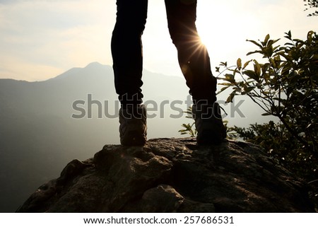 Woman hiker legs stand on mountain peak rock 