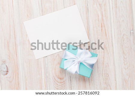 Gift box and blank photo frame or greeting card on white wooden table. Top view