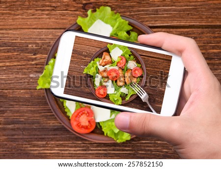 Hands taking photo vegetable salad with meat with smartphone