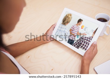 Smiling young designer presenting ideas to colleagues against close up of a tablet pc and a mug of coffee