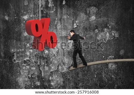 Businessman balancing on wooden board with red percentage sign and mottled concrete wall background