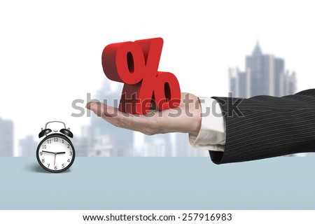 Hand showing 3D red percentage sign with alarm clock and cityscape background