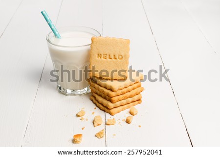 Milk and cookie with HELLO sign against white wooden background 