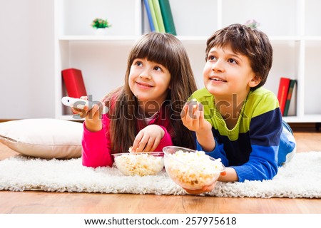 Little girl and little boy enjoy eating popcorn and watching tv at home.Leisure time for children Royalty-Free Stock Photo #257975618