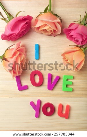 Beautiful roses with phrase "I Love You" on wooden table background