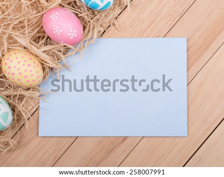 Decorated Easter eggs next to a blank envelope for copy spaceon a wood background