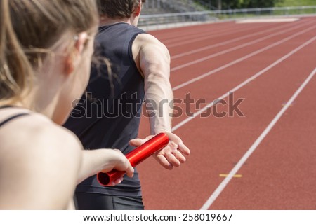 Relay race handing over from woman to man. Unfiltered version Royalty-Free Stock Photo #258019667