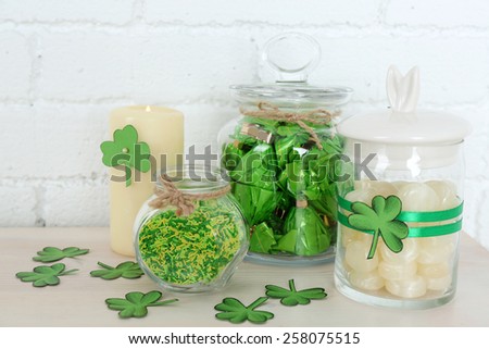 Sweets in jars for St Patrick Day on table on brick wall background