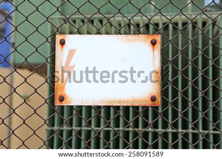 Electricity sign with empty label over a metallic fence. Put text at your own