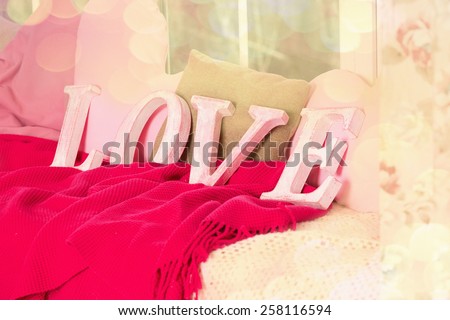 Wooden letters of the word Love. four letters make up the word Love stand against the light from the window and bokeh. Blankets, pillows, soft, light, comfort, warmth up the atmosphere of love. Retro.
