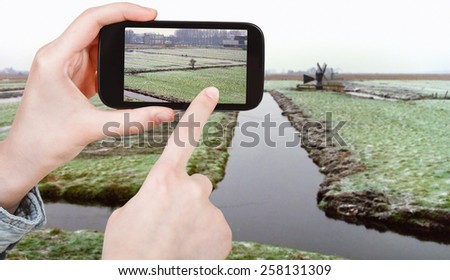 travel concept - tourist taking photo of frozen canals in Netherlands in winter on mobile gadget