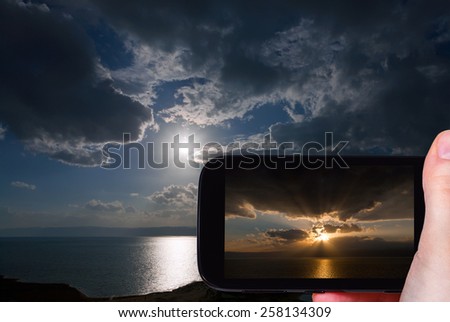 travel concept - tourist taking photo of sunset on Dead Sea on mobile gadget, Jordan