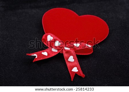 Red heart with silk ribbons macro isolated on black velvet background.