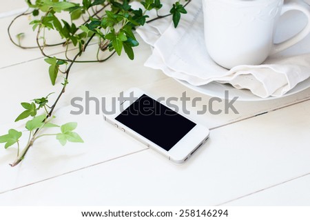 White smartphone, plants and ceramic cup on a white wooden table