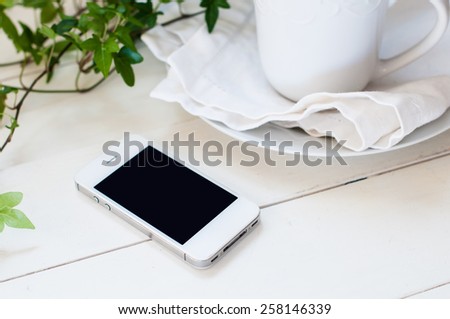 White smartphone, plants and ceramic cup on a white wooden table