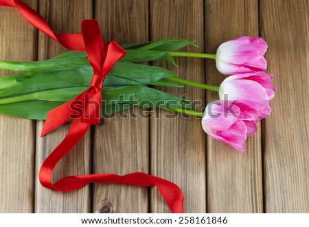 Top view of pink tulips with red ribbon and bow on wooden background
