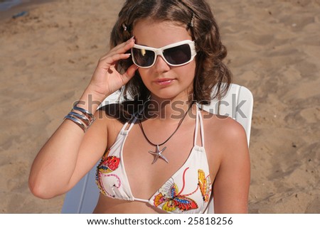 a beautiful smiling girl in sunglasses sits on lounge on the beach