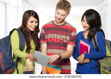 Group of happy young teenager students standing and smiling with books and tablet