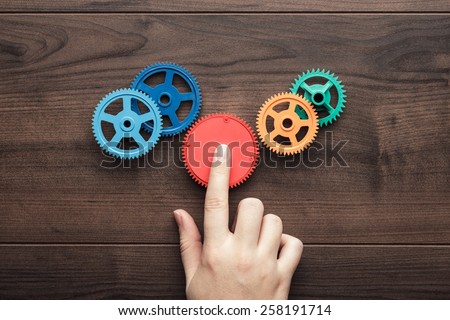 perfect solution concept. colorful gears and hand on the brown wooden background Royalty-Free Stock Photo #258191714
