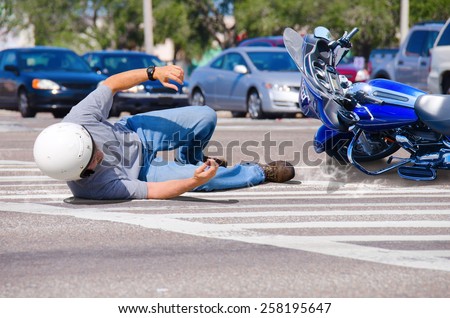 Motorcycle rider has wrecked and is laying in the road as his motorcycle goes sliding into the busy intersection.  Royalty-Free Stock Photo #258195647